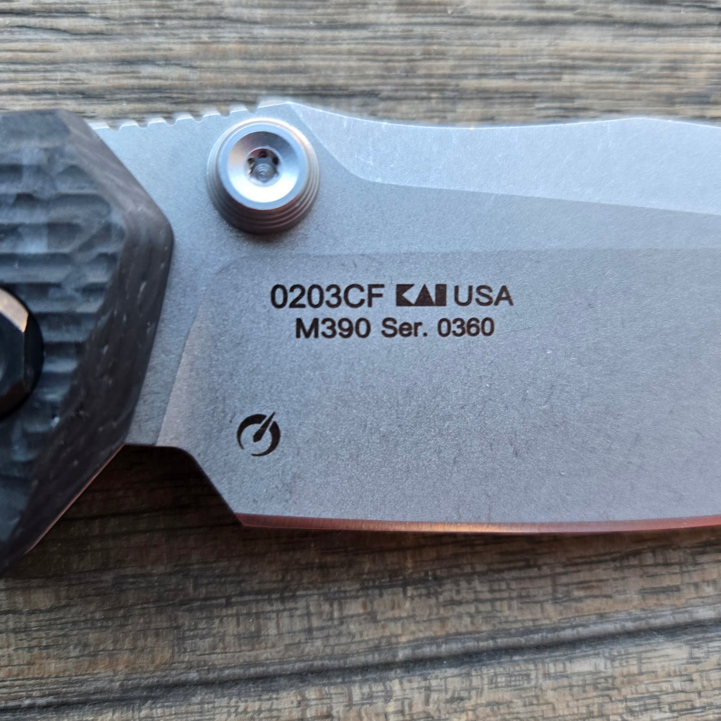Close-up of a folding knife blade with branding and model number on a wooden surface